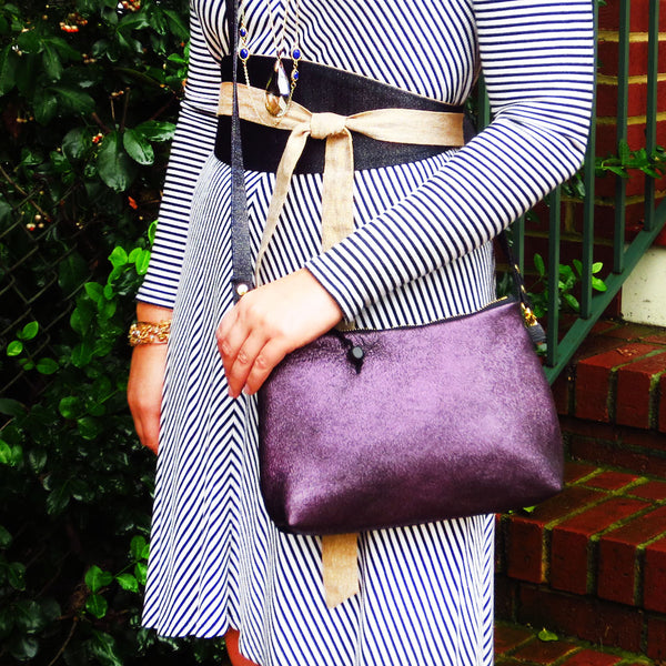 Emily is wearing the raina crossbody bag in purple leather, and the selina wrap belt in denim and gold essex linen.