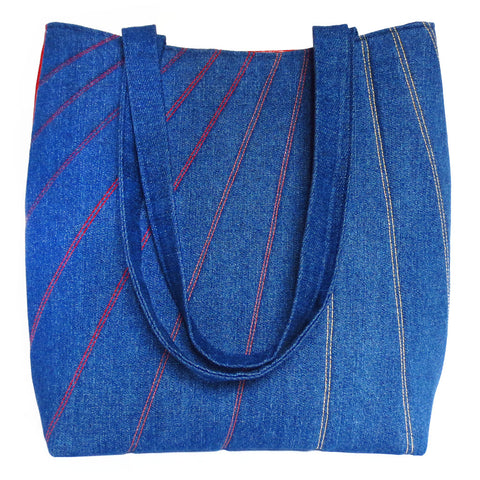 dark blue denim tote stitched with lines in shades of red, orange, and gold. back is red vinyl.