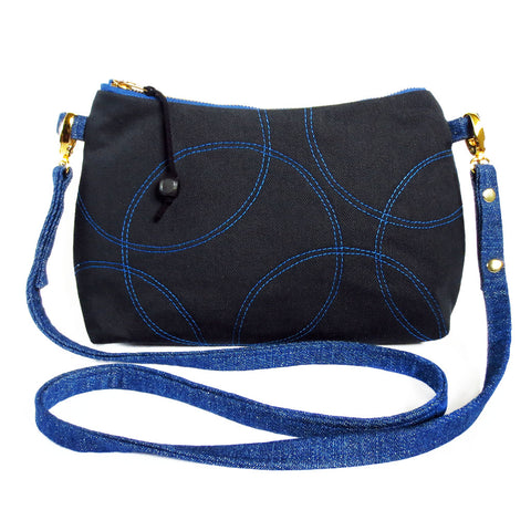 Crossbody bag in black and blue denim. Front is stitched in overlapping circles motif in blue thread on black. 
