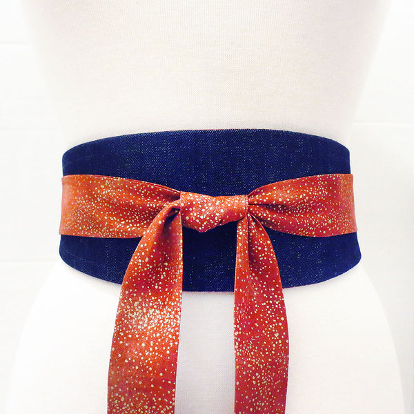 the Josephine wrap belt wrapped to show the denim side flecked with gold. Long ties in red and gold print are tied in a knot in the center front.
